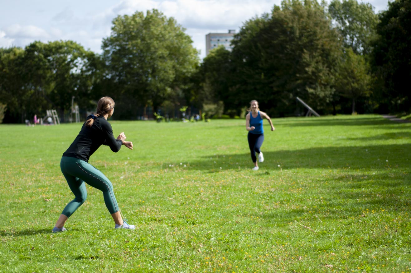 Girl running with Personal Trainer motivating and timing her outdoors in the park